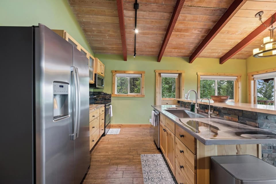 Gather in your chef-ready kitchen, where natural wood and exposed beams meet modern appliances. Sunlight streams through large windows, inviting you to cook and connect surrounded by mountain greenery.