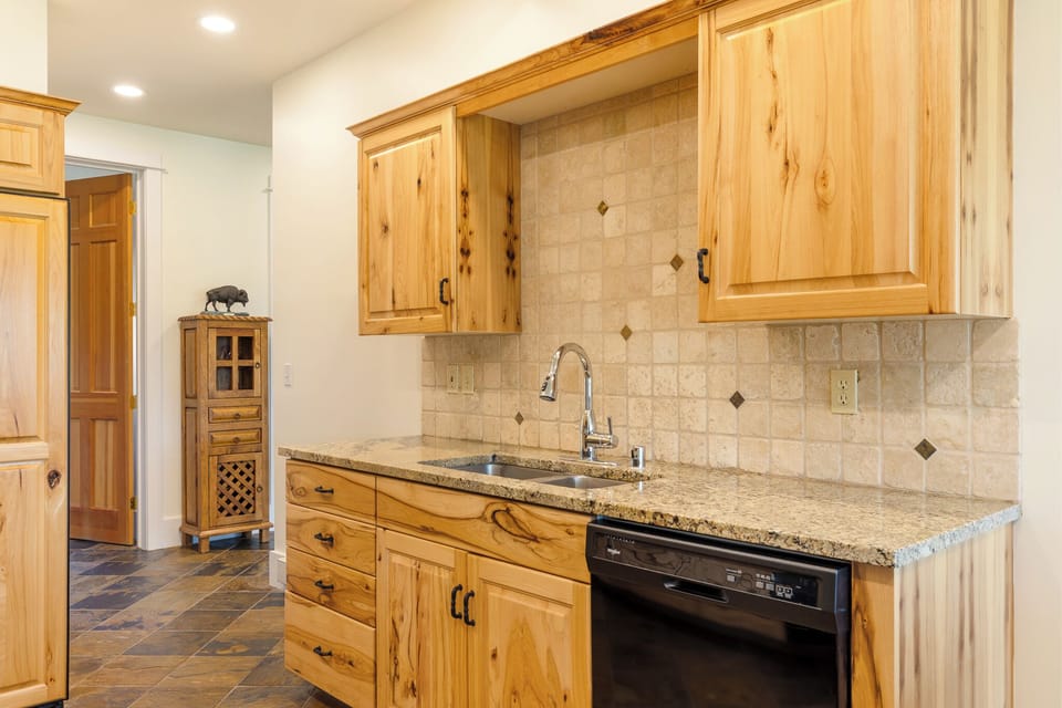 Your kitchen features warm natural wood cabinetry, granite countertops, and a neutral stone tile backsplash—everything you need to prepare your favorite meals in style.