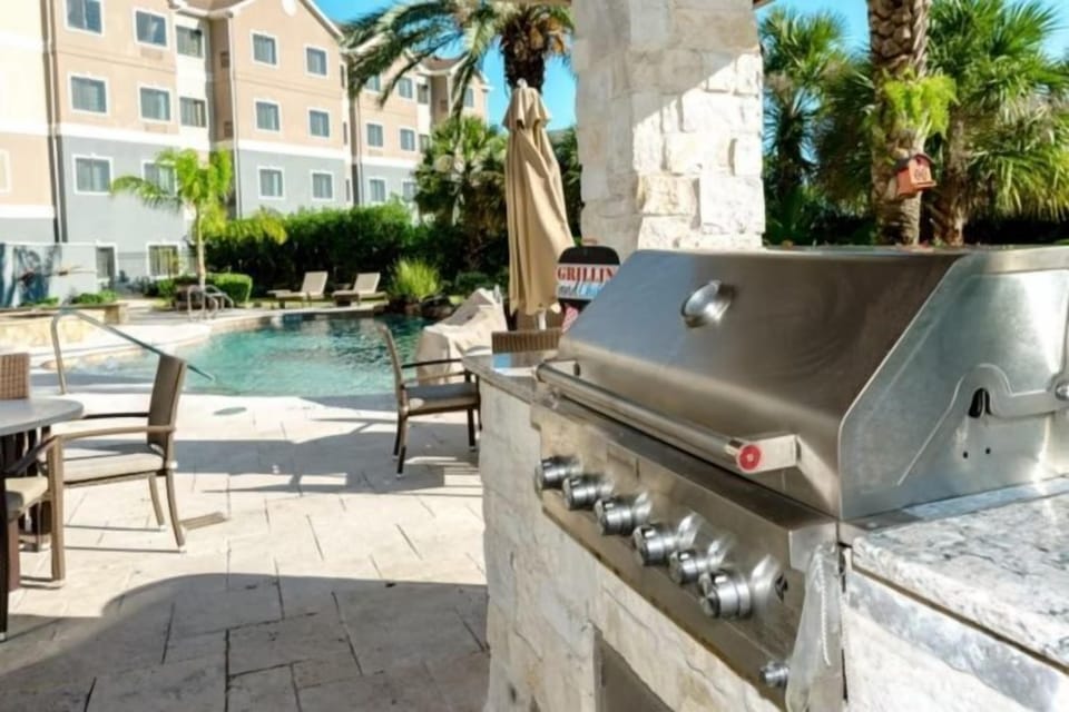 Outdoor BBQ grill with poolside seating and palm trees
