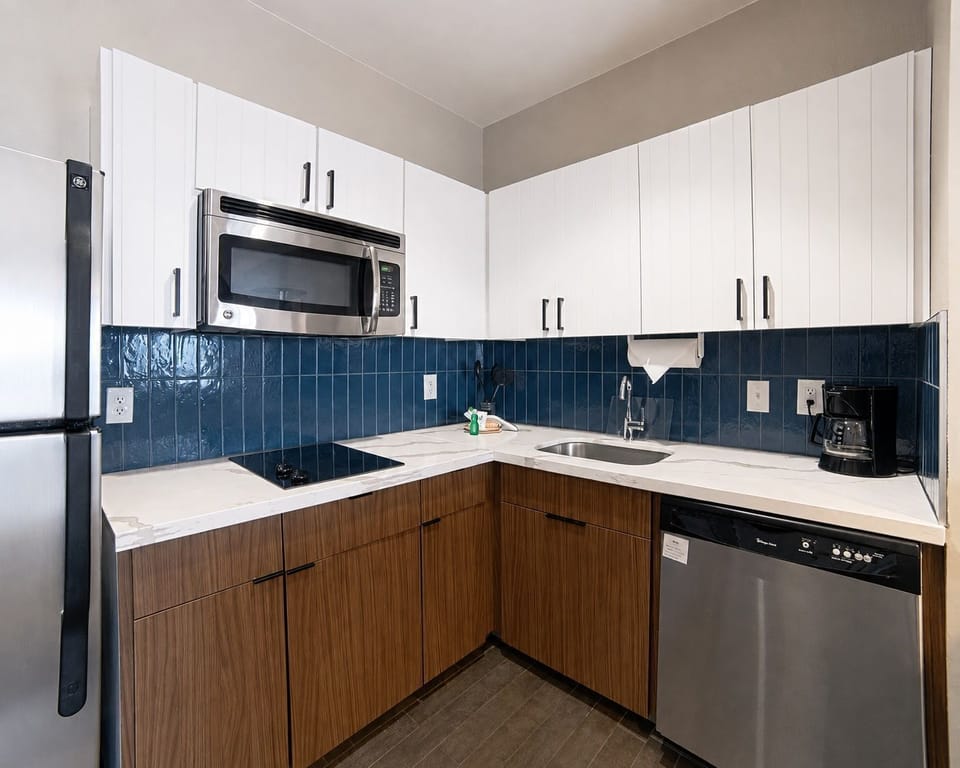 Compact kitchen with blue tile backsplash, refrigerator, and microwave.