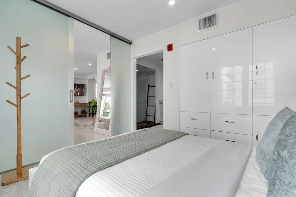 Thoughtfully designed bedroom with sleek built-in wardrobes, soft layered bedding, and frosted-glass sliders connecting to the living space — modern comfort meets smart design in this South Beach hideaway.