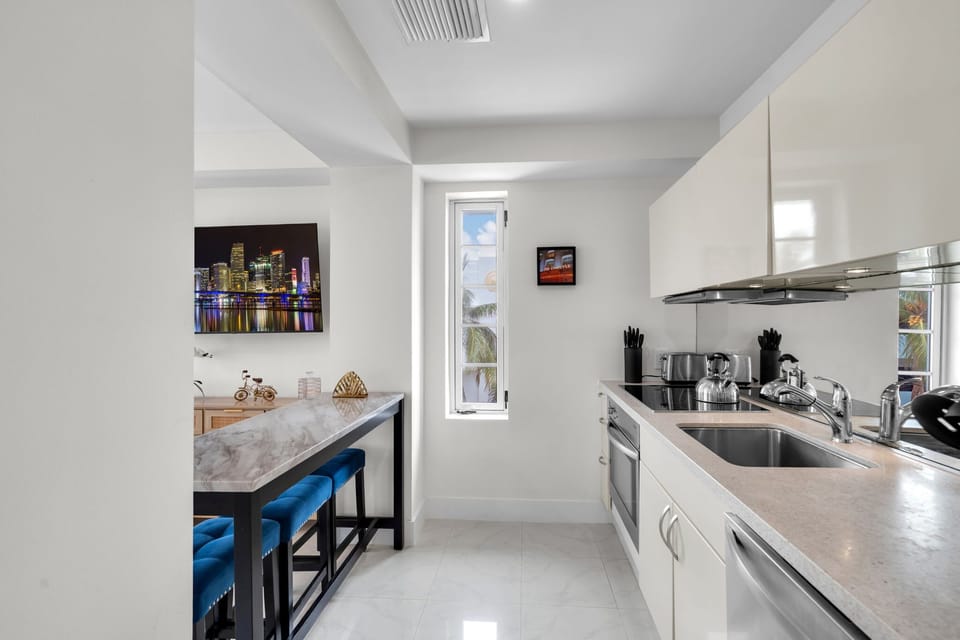 Sleek, fully equipped kitchen with glossy white cabinetry, stainless appliances, and everything you need to cook like home — from quick breakfasts to full dinners, all just steps from South Beach dining.