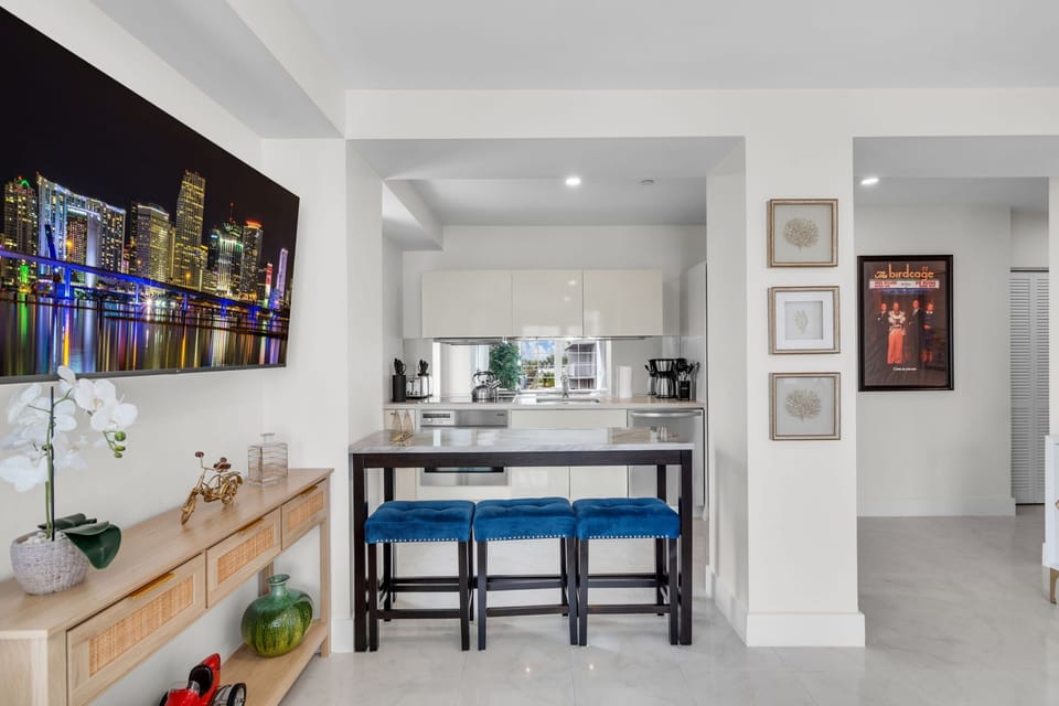 Stylish breakfast bar with vibrant blue velvet stools and a striking Miami skyline canvas — the perfect spot for morning coffee or evening cocktails, right beside the fully equipped modern kitchen.