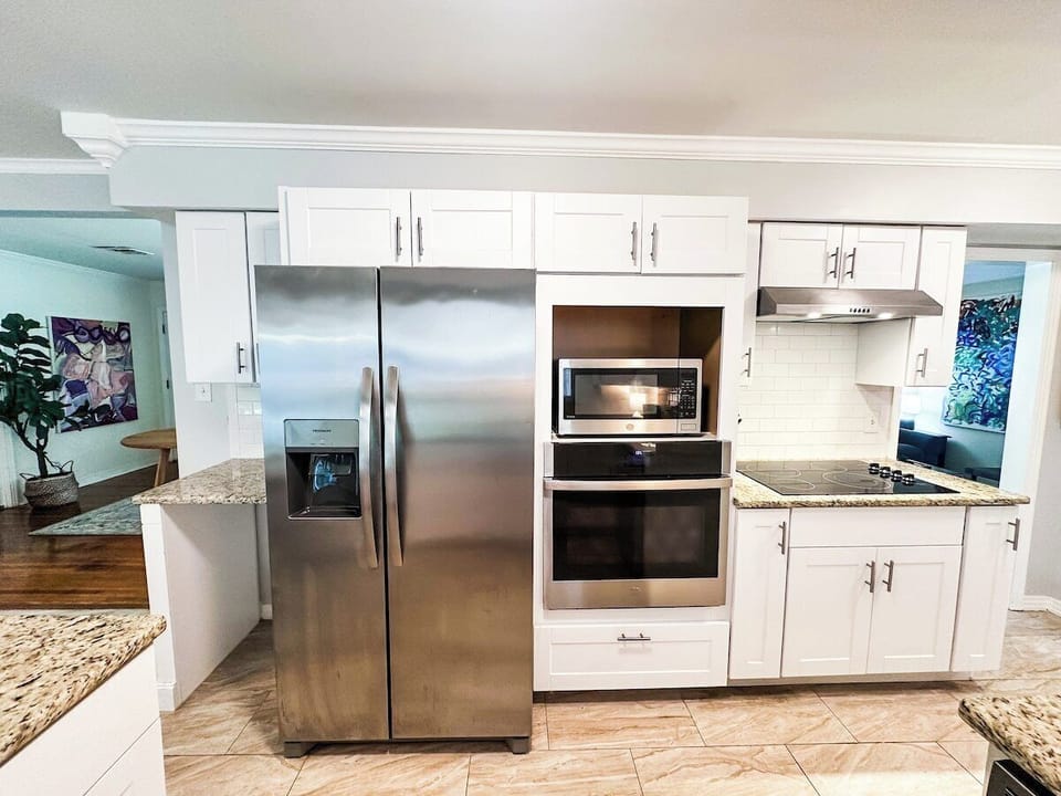 Prepare meals with ease in this bright kitchen, featuring crisp white cabinetry, granite countertops, modern stainless steel appliances including a double-door refrigerator, built-in microwave and wall oven, and a sleek glass cooktop.