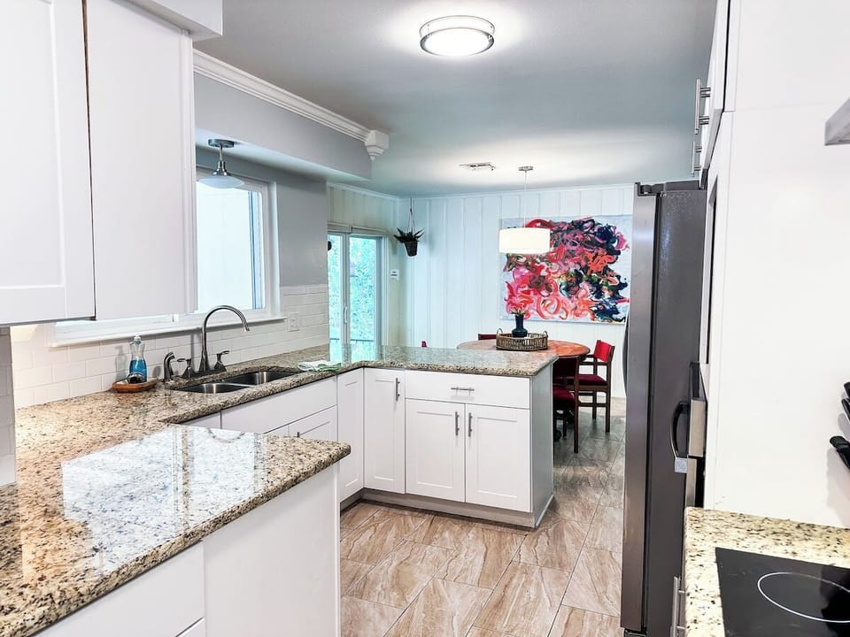 Cook and entertain in this bright, open-concept kitchen featuring white shaker cabinets, granite countertops, an undermount sink, and stainless steel appliances, leading directly into an adjoining dining area.