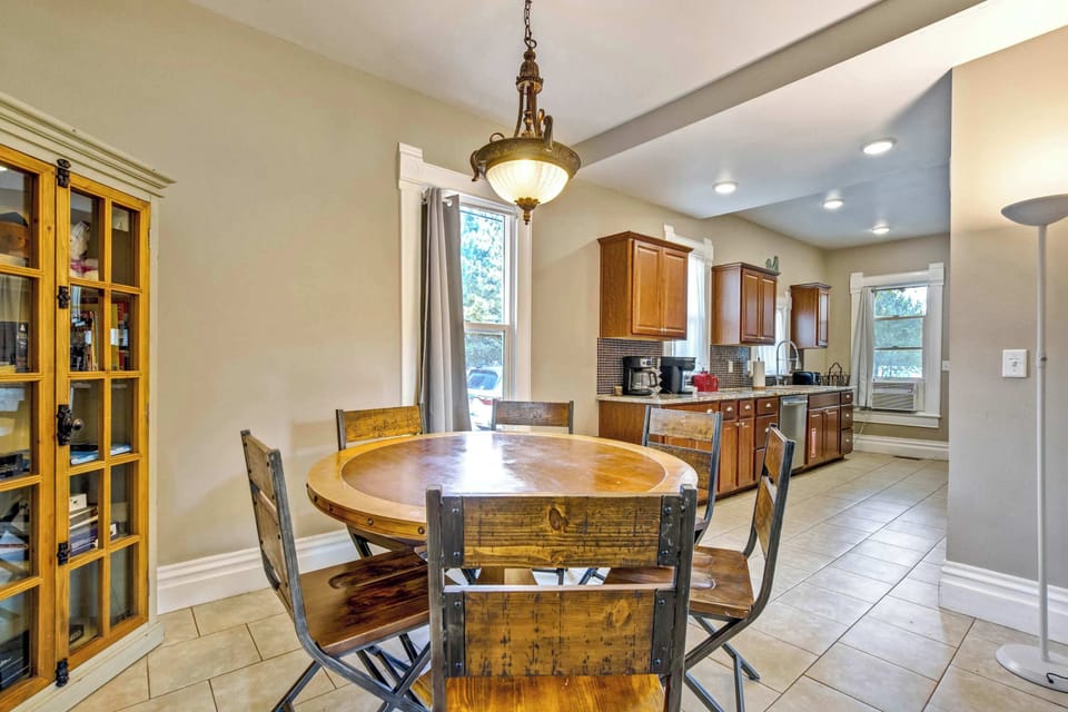 A round wood dining table sits beneath an ornate pendant light fixture beside a built-in cabinet with glass front doors, with open sightlines through to the kitchen so that the cook never gets left out of the conversation.