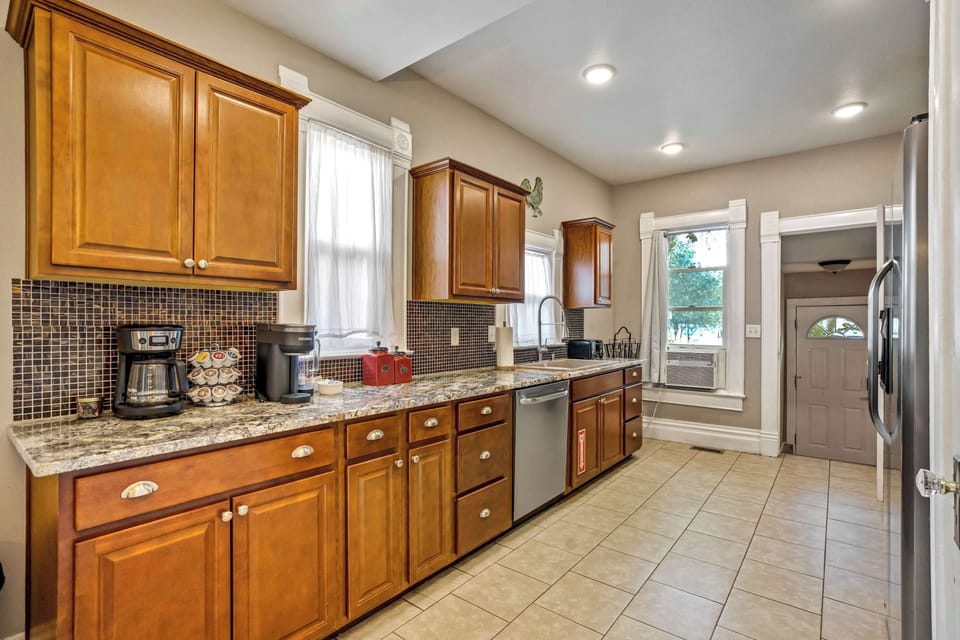 The galley kitchen pairs warm wood cabinetry with speckled granite counters and a dark mosaic tile backsplash, lit by recessed lighting overhead. A complimentary coffee station with pods sits ready on the counter each morning.