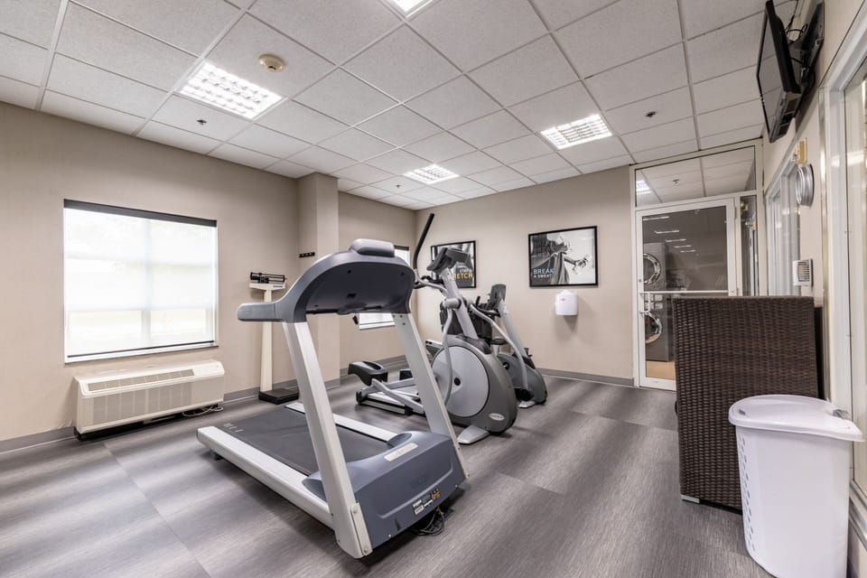 Fitness centre with treadmill and elliptical machine beside large windows.