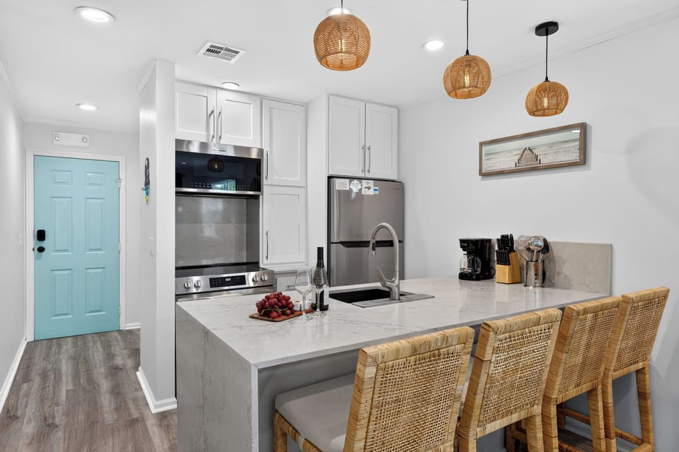 Modern kitchen with white cabinetry, stainless steel appliances, and a breakfast bar with wicker stools.