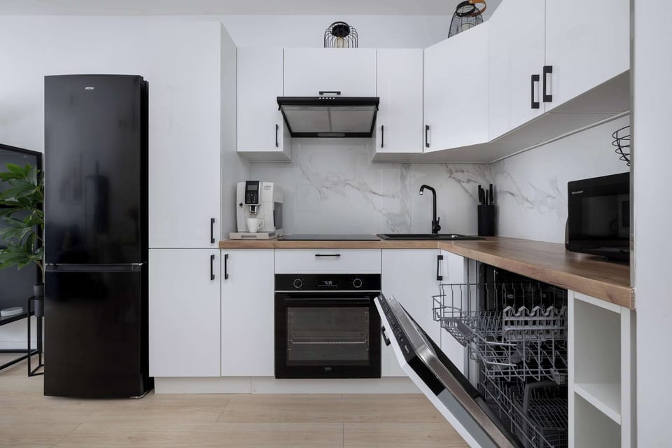 Modern kitchen layout showing open cabinet doors and a dishwasher. White cabinetry extends around the corner next to a freestanding black refrigerator.
