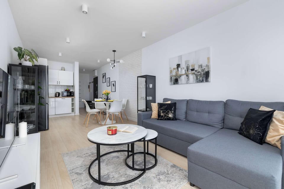 Open-plan living space combining a dining set in the foreground with a comfortable sofa set in the background. Modern lighting illuminates the light-toned wooden flooring throughout.