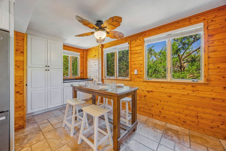 Gather for meals in your bright, cozy dining nook with rustic wood walls, warm natural light, and serene tree views framing every bite.
