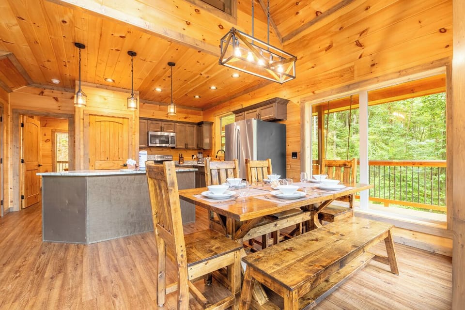 Bright, open cabin with warm wood tones and expansive windows. Handcrafted dining table overlooks lush forest views—your peaceful escape awaits.