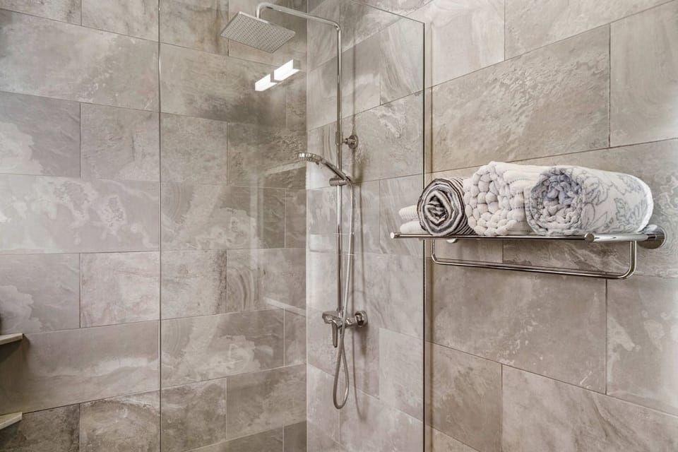 Modern walk-in shower with sleek gray stone tile and a rainfall showerhead.