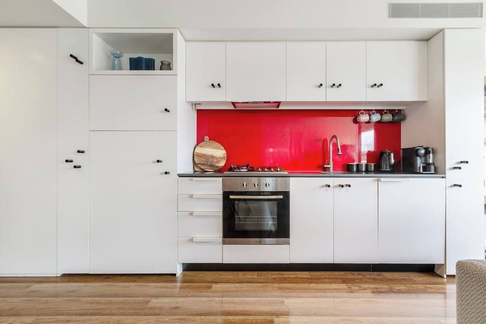 A bold red splashback brings playful energy to the sleek kitchen, complete with a gas cooktop, oven, full-size refrigerator, and all the essentials for effortless home cooking.