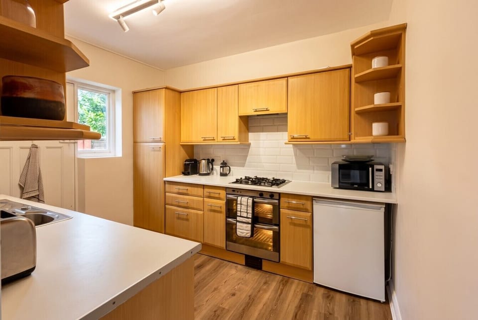 The kitchen fitted with wooden cabinets, white worktops, a gas hob and oven, microwave, fridge, and a range of countertop appliances including a coffee machine and kettle.
