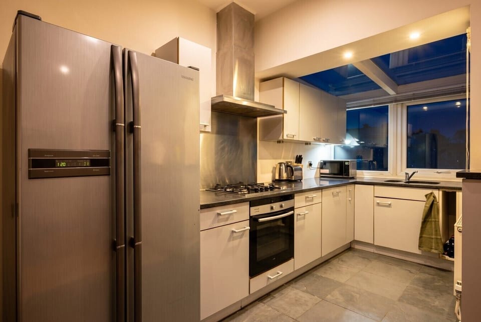 Sleek kitchen with American fridge and skylight, glowing warm at dusk.