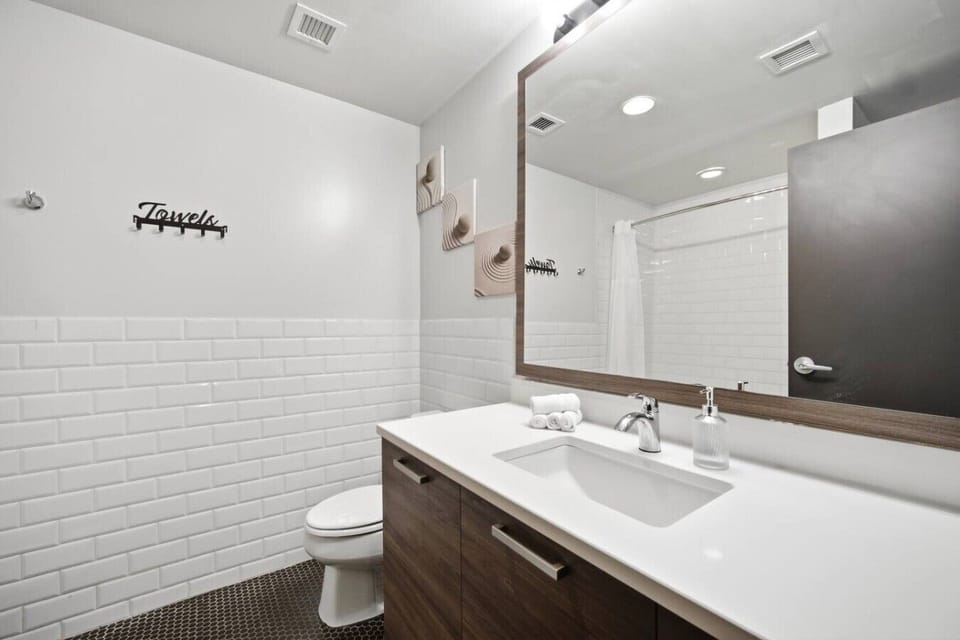 Serene apartment bathroom featuring a vanity with white countertops, a large mirror, white subway tile walls, a toilet, and a tiled shower stall with a curtain.