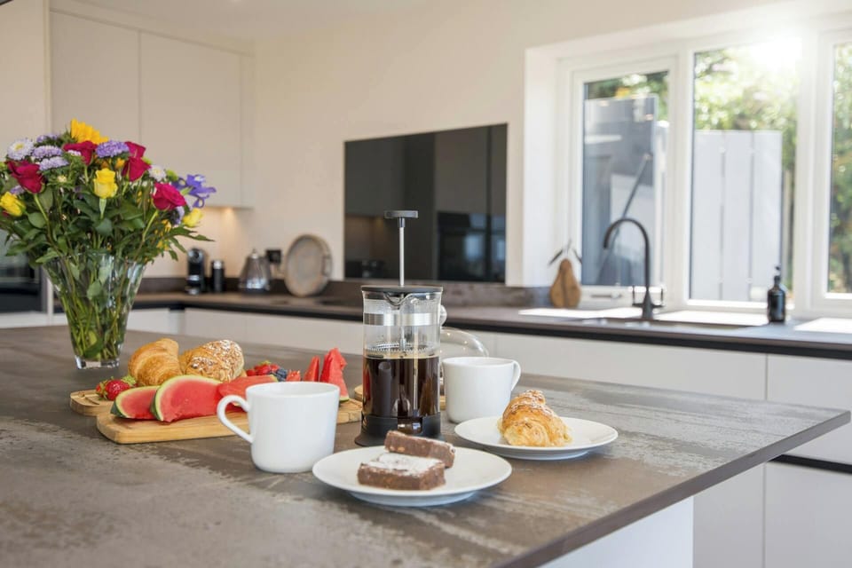 Breakfast spread with coffee press, mugs, pastries and fruit on a kitchen island