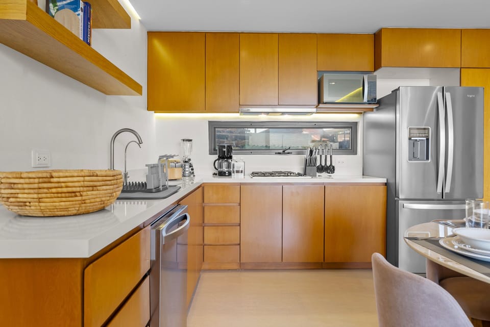 L-shaped gourmet kitchen featuring warm wooden cabinetry, polished quartz countertops, stainless steel appliances, under-cabinet lighting, floating shelves, and small countertop appliances.