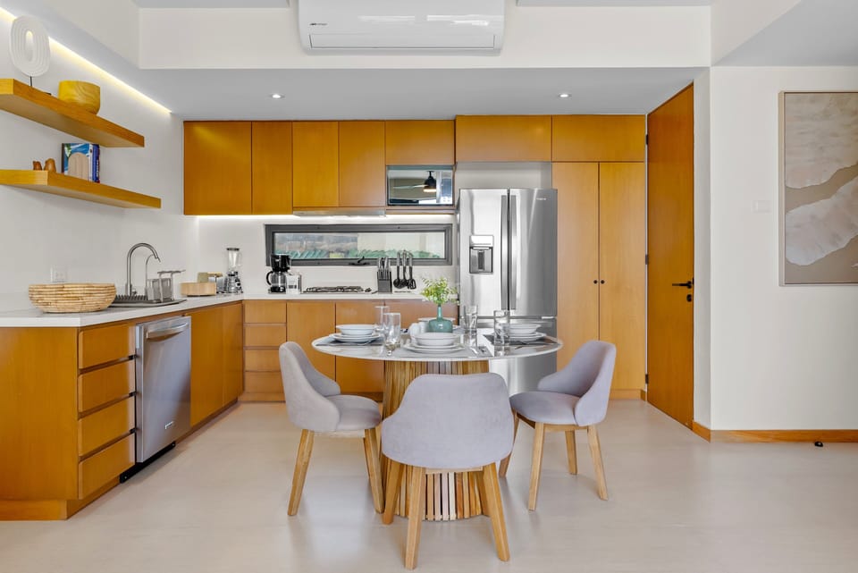 Fully equipped modern kitchen highlighting warm wood cabinetry, stainless appliances, floating display shelves, and a elegant round dining table setup for entertaining family and guests in style.