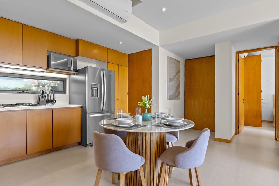 Full kitchen featuring custom warm wood cabinetry, stainless steel appliances, and an adjacent round dining table with elegant upholstered chairs, creating an inviting space for fine dining at home.