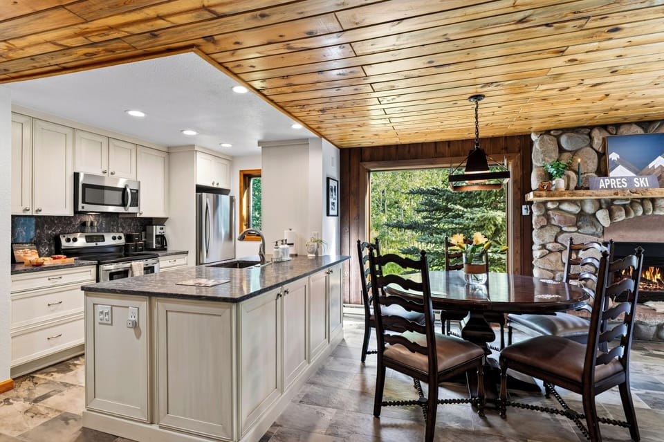 Cook and dine beside the stone fireplace, with forest views adding to the warm mountain atmosphere.