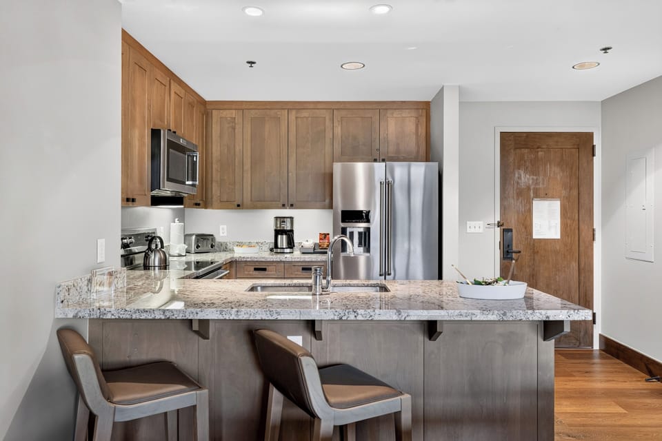 A fully equipped kitchen features granite counters, stainless steel appliances, and breakfast bar seating for casual meals.