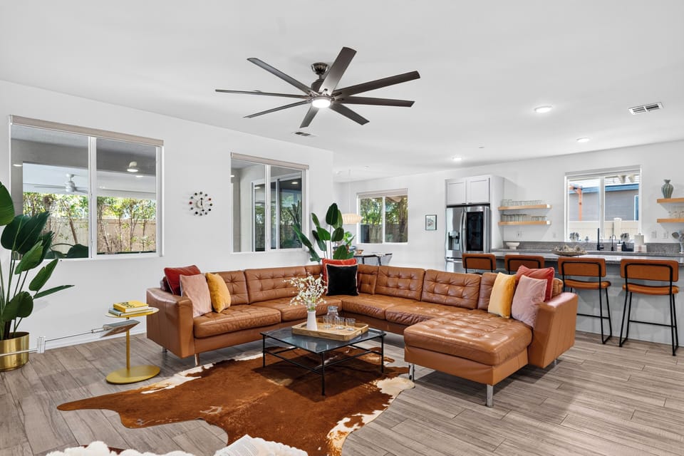 Spacious open-concept living area featuring comfortable leather sofas, a ceiling fan, and a large TV.