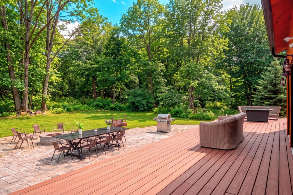 Relax on the expansive deck with multiple lounge areas and peaceful woodland views stretching beyond the patio.