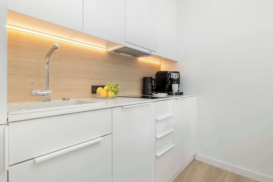 A linear white kitchen section features under-cabinet LED lighting over a light-colored countertop. A coffee maker sits in the corner.