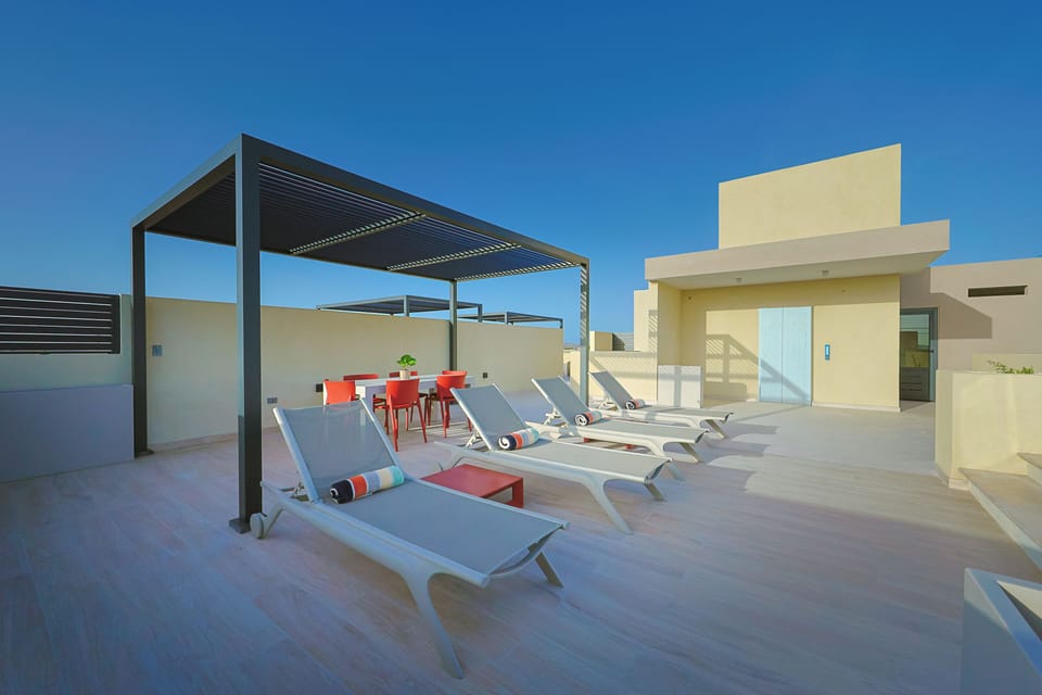 Modern rooftop terrace featuring sun loungers and a shaded dining area set against a bright blue sky—the perfect spot to unwind in style.