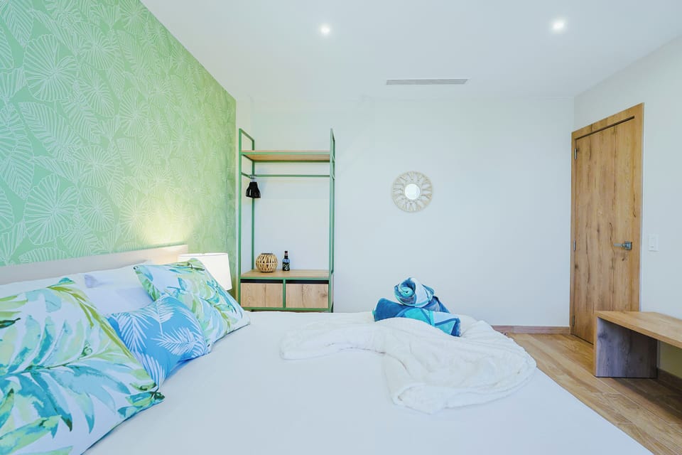 Unwind in your serene retreat with fresh tropical accents and crisp white linens. The soothing palm-patterned wall and airy design create a peaceful oasis for restful nights.