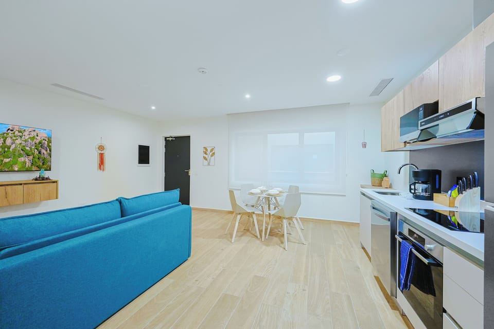 Step into your bright, modern open-plan living space where a vibrant turquoise sofa invites you to unwind. The sleek kitchen is ready for your morning coffee and home-cooked meals.