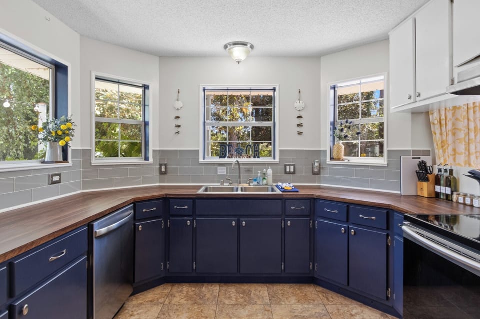 Cook up fresh catches in this bright, breezy kitchen with navy cabinets, wood counters, and windows framing leafy green views.