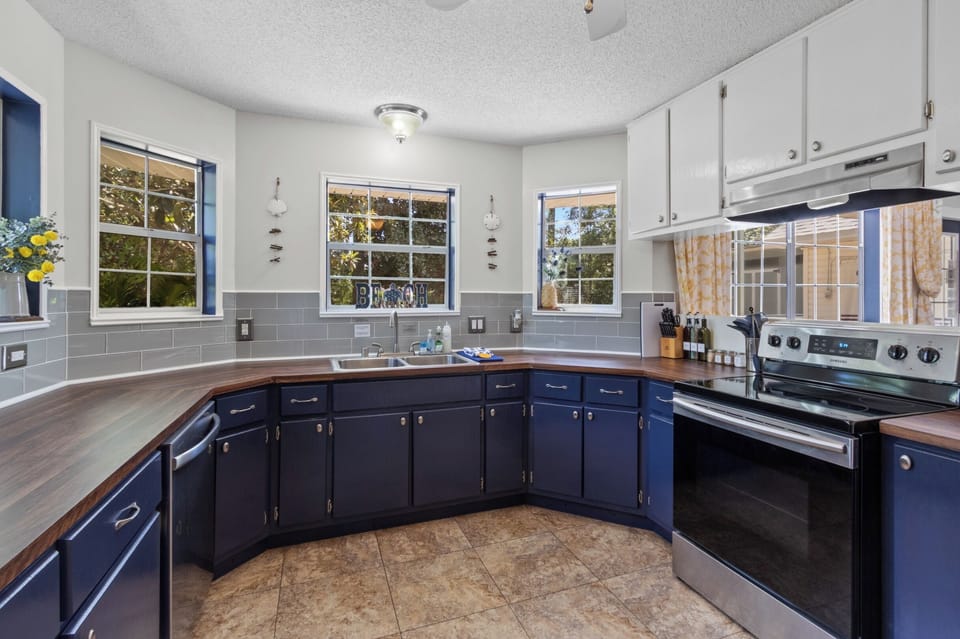 Cook up fresh catch in this sunny, coastal kitchen with navy cabinets, butcher-block counters, and stainless appliances ready for your stay.