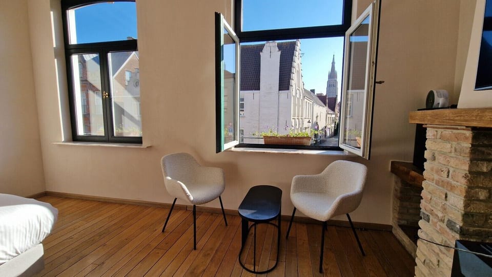 Room to breathe: a seating corner by the window, a desk that doubles as a vanity table, and Bruges` rooftops and cathedral as your backdrop.