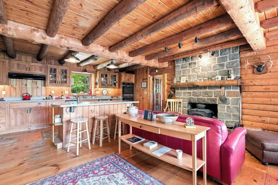The kitchen island and long dining table share the space with a stone fireplace, keeping cooking and gathering all in one open room.