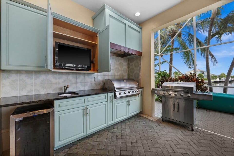 Waterfront outdoor kitchen with grill, TV, and tropical screened views