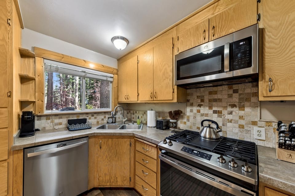 Corner kitchen with oak cabinets, stainless steel appliances, double sink, and tiled backsplash featuring bear motifs.