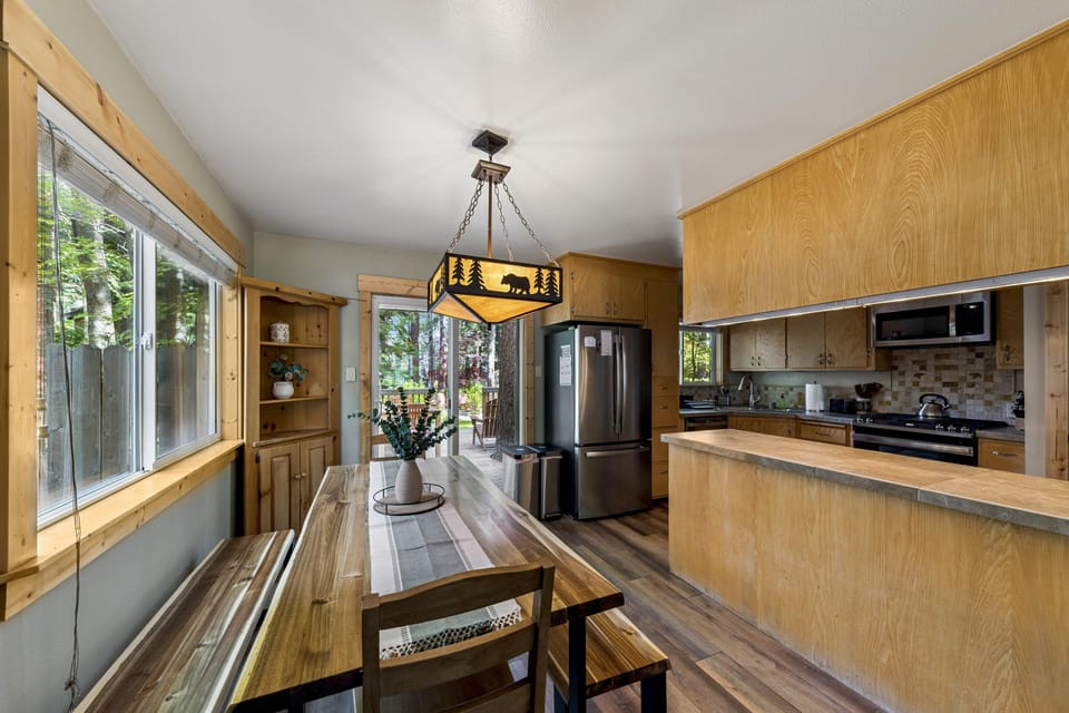 Dining area with a live-edge wood table, bench seating, bear-themed pendant light, and sliding glass door to the deck.