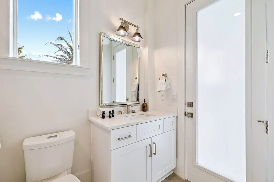 Bright full bathroom with sleek white vanity, gold accents, and direct outdoor deck access.