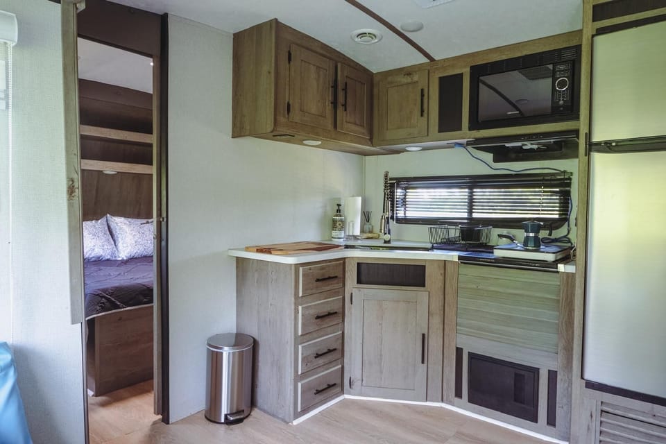 Inside kitchen, electric stove top, microwave, fridge and sink.  Bedroom door.