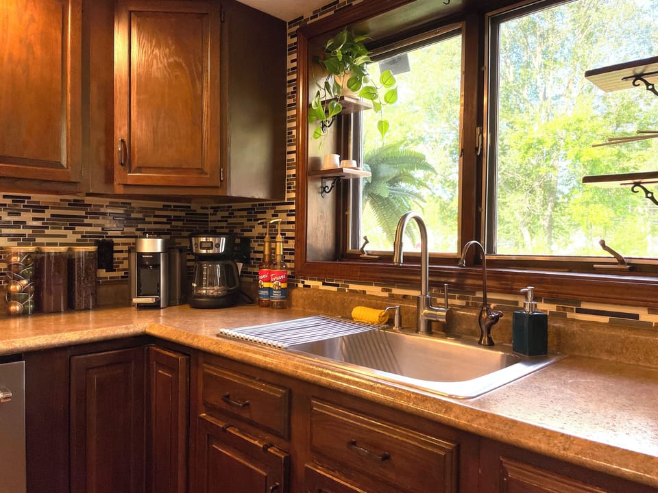 Even your kitchen cleanup comes with a leafy view 🌿, plus a double sink and both pod and drip coffee makers waiting nearby.