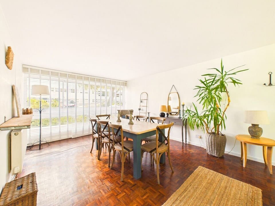 A generous six-seater dining table sits under a wall of windows, ready for long lunches after a day exploring the Cotswolds.