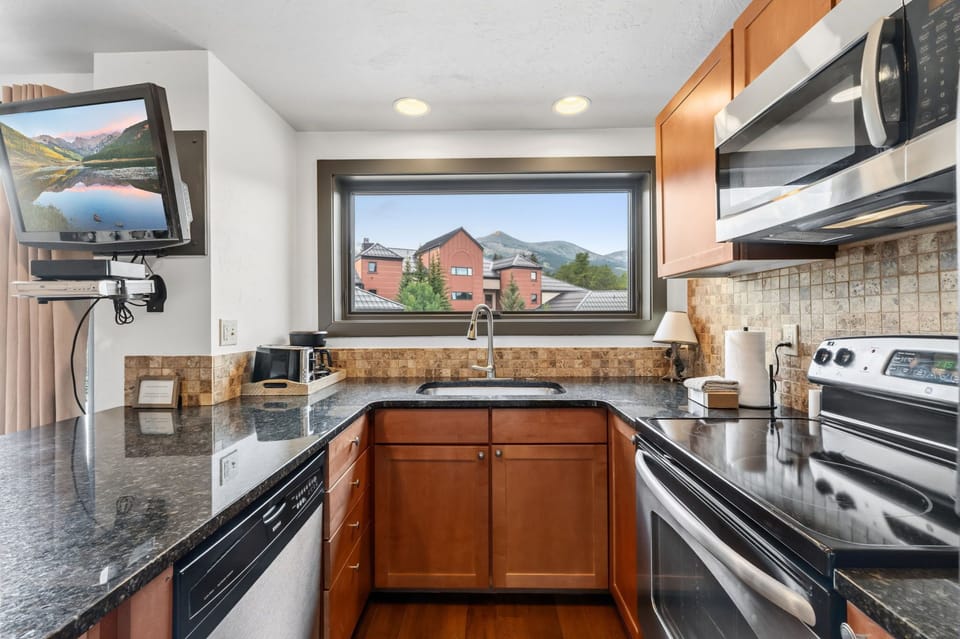 Your fully-equipped kitchen features sleek granite countertops, modern stainless steel appliances, and a window framing peaceful mountain views—perfect for preparing meals while soaking in the scenery.