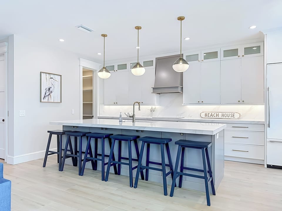 Gather around this spacious kitchen island with crisp white countertops, coastal charm, and stylish seating for group meals and morning coffee.