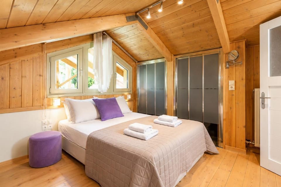 A rustic attic bedroom features wood-paneled walls and ceilings, a double bed with purple accent pillows, and tracking lights illuminating the sloped space.