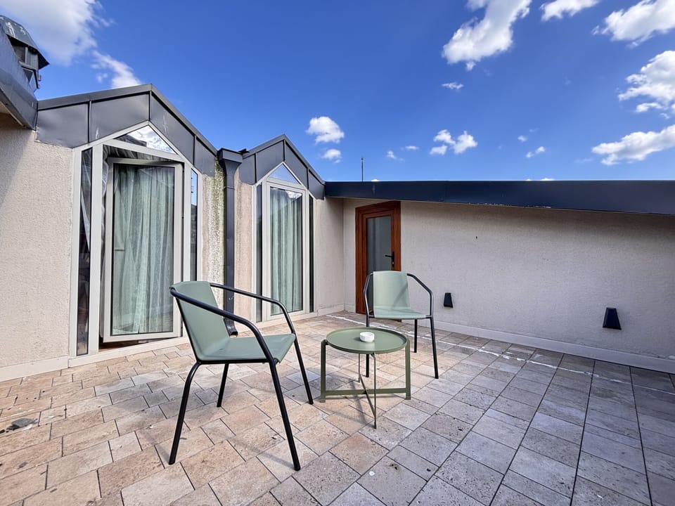 Terrace with two chairs, a round table and rooftop windows.
