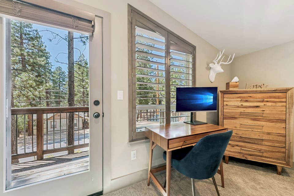Primary bedroom upstairs - Bright workspace with rustic wood furniture and forest views framed through large glass doors—natural light floods your desk while you settle in for work or relaxation.